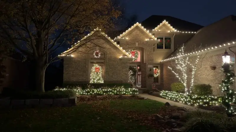 A two-storey home lit with white lights along its rooflines, wreaths in the windows